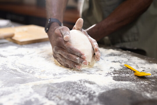African American man shaping dough ball on floured kitchen counter with yellow scraper