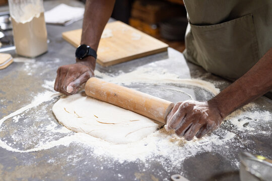 African American man rolling dough on kitchen counter wearing green apron, using rolling pin
