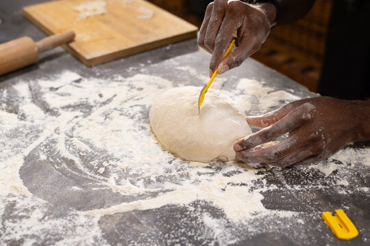 African American man in dark long-sleeve steadying and scoring dough in kitchen with yellow tool