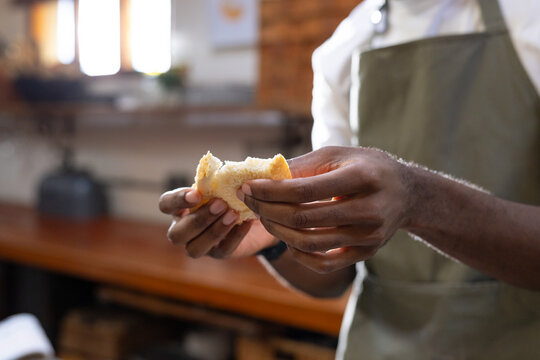 African American man tearing roll with both hands at kitchen counter wearing olive-green apron