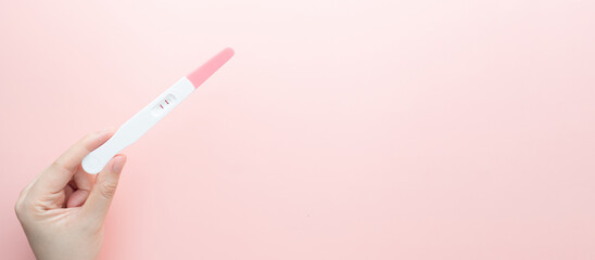 Pregnant woman holding a positive urine pregnancy test on pink background. Pregnancy test kit measure hCG levels in urine. © Orawan