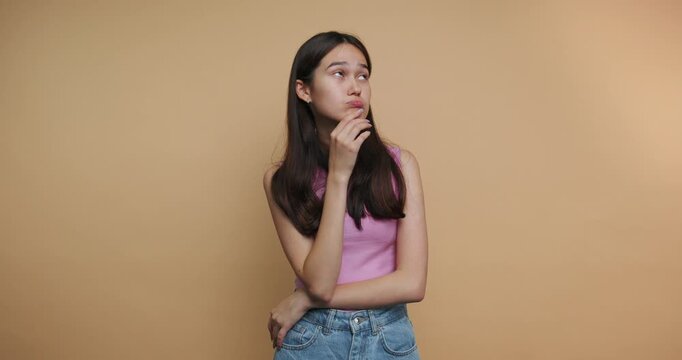 Girl poses in front of orange wall showing different expressions and holding finger to chin while thinking about something