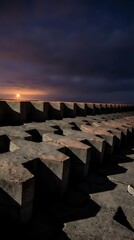Fototapeta premium Concrete breakwater blocks arranged in rows along sandy beach at sunset with dramatic cloudy sky and golden light reflecting on water.