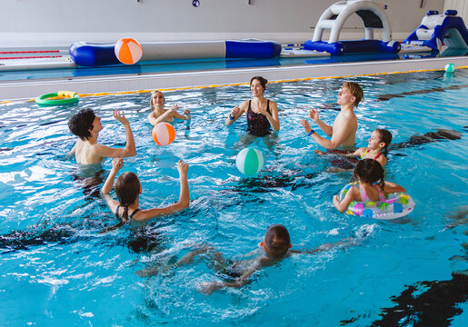 Large group of friends and family with children playing water volleyball with inflatable balls in an indoor pool