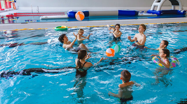 Large group of friends and family with children playing water volleyball with inflatable balls in an indoor pool