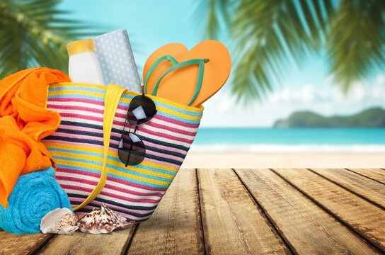 Striped beach bag with summer accessories on a wooden table with tropical sea background
