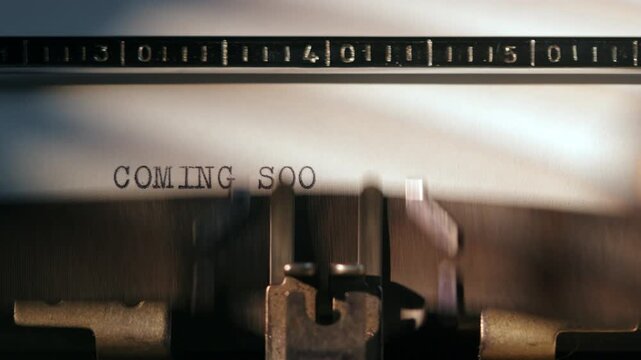Typing a message on a typewriter showing the words coming soon on a page with a ruler beside it