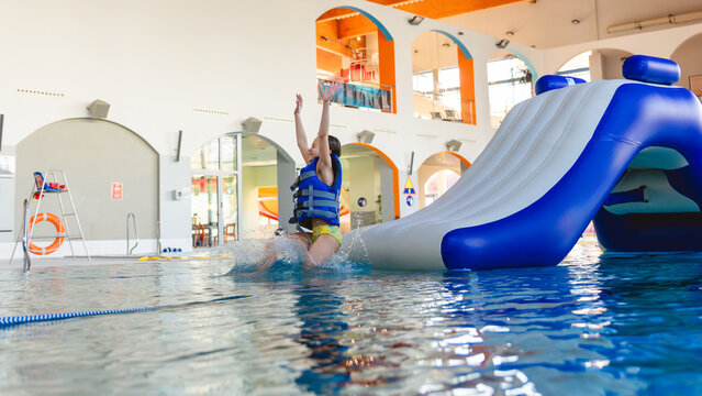 Young girl wearing a life vest sliding down a large inflatable water slide into an indoor swimming pool