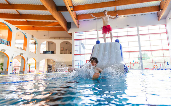 Two young men having fun on an inflatable water slide in an indoor swimming pool