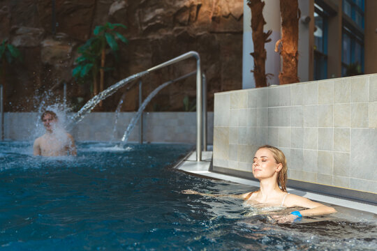 Beautiful young blonde woman relaxing with eyes closed in an indoor swimming pool with water fountains