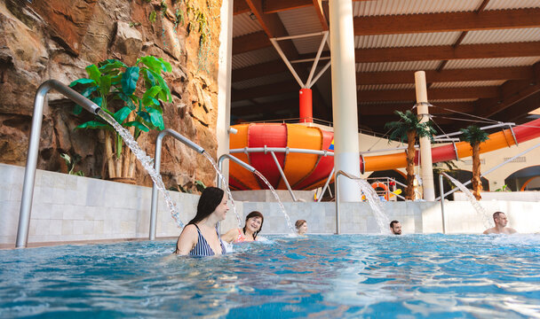 Happy mature woman relaxing with friends under a water fountain in an indoor swimming pool at a water park