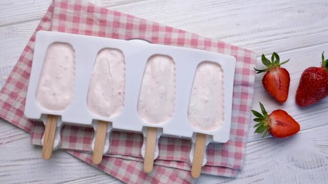 Preparing homemade strawberry popsicles on wooden table