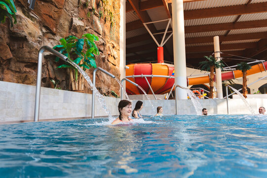 Happy mature woman relaxing with friends under a water fountain in an indoor swimming pool at a water park