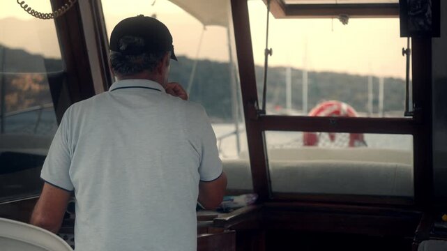 Boat captain navigates waters during sunset near harbor with sailboats in the background