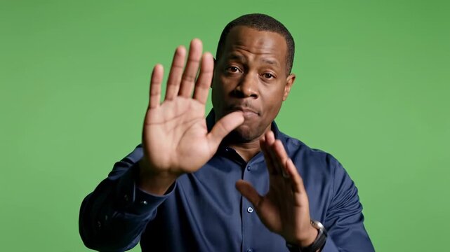 Man gesturing stop and warning sign on green screen background, male person african