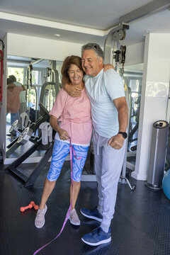 Couple with mature man and senior woman smiling, posing in workout clothes holding pink band