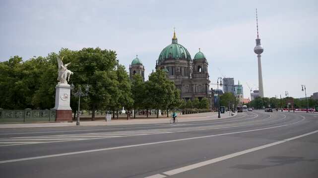The Berlin Cathedral and Fernsehturm appear beyond linden trees and a broad road. Historic architecture, monuments and quiet traffic shape the city panorama.