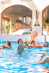 Naklejka premium Happy young male friends playing with a beach ball in a large indoor swimming pool at a water park