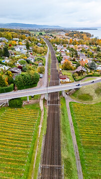 Aerial view of railway tracks passing through residential neighborhoods and lush vineyards near Lake Geneva in Crans, Vaud, Switzerland.