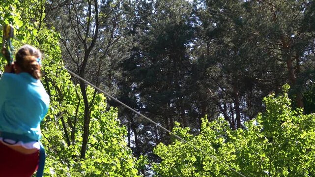 Beautiful girl in an blue blouse rides rope. Zip line, zip-line, zipline, zip wire, or aerial runway, is pulley suspended on cable, usually made of stainless steel, mounted on slope.