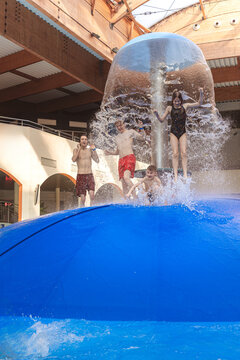 Group of happy people jumping from a blue water mushroom fountain dome at an indoor water park