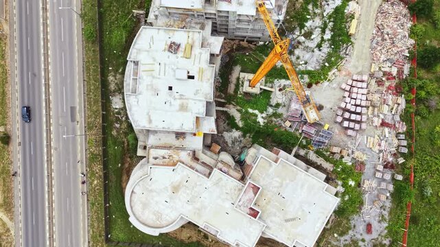 Aerial construction site view with concrete foundations, tower crane, scattered rubble, adjacent highway with moving vehicles, earthwork machinery, exposed