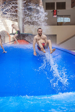 Group of happy people jumping from a blue water mushroom fountain dome at an indoor water park