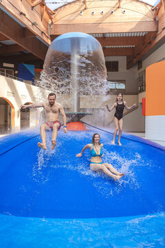 Group of happy people jumping from a blue water mushroom fountain dome at an indoor water park