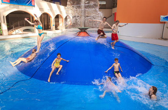 Large group of happy people jumping from a blue water mushroom fountain dome at an indoor water park