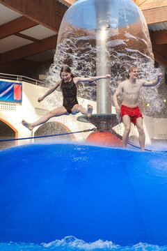 Group of children jumping from a blue water mushroom fountain dome at an indoor water park