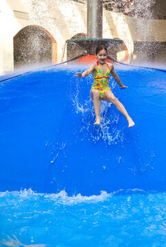 Group of children jumping from a blue water mushroom fountain dome at an indoor water park