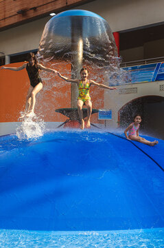 Group of children jumping from a blue water mushroom fountain dome at an indoor water park