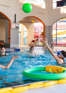 Group of happy children playing with a green inflatable ball in an indoor swimming pool