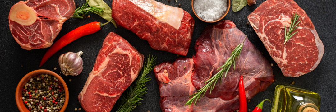 Various cuts of beef steak are shown with herbs, spices, and oil on a dark surface. Perfect for those looking to prepare or grill different beef dishes at home, banner