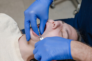 Orthodontist hands in blue gloves examining upper jaw braces on relaxed teen patient with eyes closed in dental chair. Overhead view of bracket inspection with calm comfortable clinical atmosphere.... © Oksana
