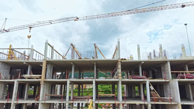 Aerial view concrete skeleton building under construction, exposed columns and rebar, cranes adorned with safety flags, crews pouring concrete and operating