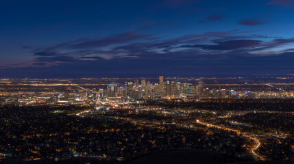 Fototapeta premium Aerial view of a city skyline illuminated at night with a dark blue sky and scattered clouds above it