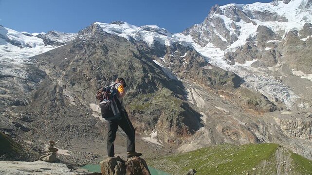 Hiker with backpack admiring glacier lake and Monte Rosa east face from alpine mountain viewpoint on a sunny summer day, trekking adventure in the Italian Alps, Macugnaga