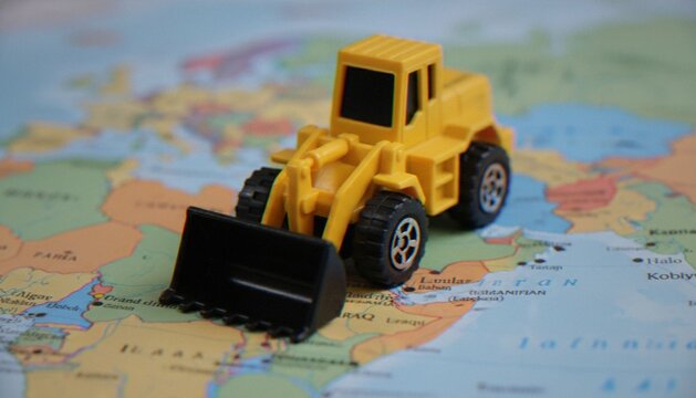 A miniature yellow toy bulldozer sitting on top of a blurred world map focusing on the Middle East region.