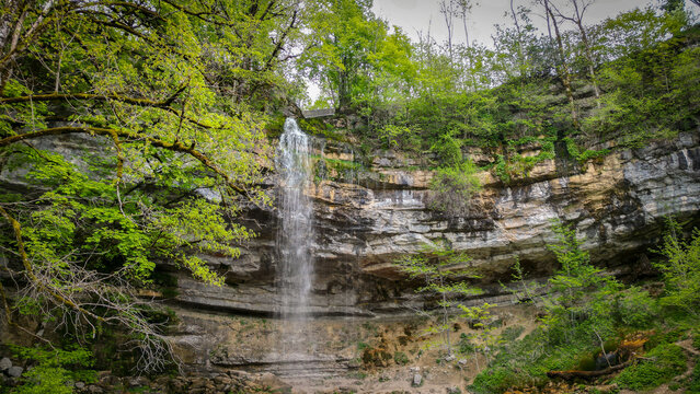 Aerial view of the Herisson waterfalls cascading down a rocky limestone cliff surrounded by lush green trees and forest in Menetrux-en-Joux, Bourgogne-Franche-Comte, France.