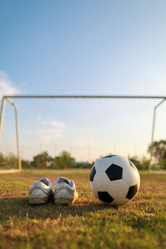 Vertical shot of a classic soccer ball and white football boots on green grass against a clear blue sky, sports background with copy space.