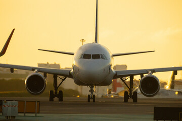 Naklejka premium Airplane taxis on runway during sunset with airport buildings in background and bright orange sky