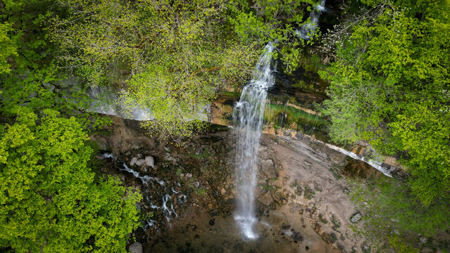 Aerial view of the Herisson waterfalls cascading down a rocky cliff surrounded by dense green forest in Menetrux-en-Joux, Bourgogne-Franche-Comte, France.