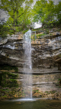 Aerial view of The Herisson waterfalls cascading down a steep limestone cliff surrounded by lush green forest in Menetrux-en-Joux, Bourgogne-Franche-Comte, France.