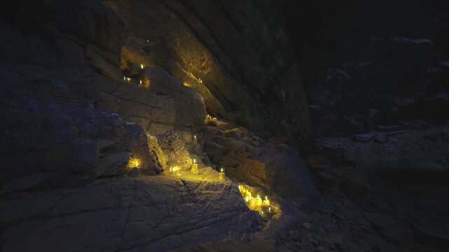 Torches along canyon at night, warm golden glow pooling on jagged rock faces, ember sparks drifting through cold air, scattered lights marking narrow trail,