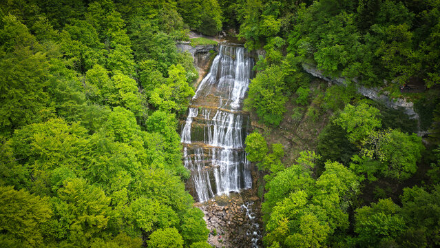 Aerial view of the Herisson waterfalls cascading down rocky tiers surrounded by a lush green forest in Menetrux-en-Joux, Bourgogne-Franche-Comte, France.