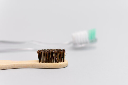 Bamboo toothbrush in foreground with blurred plastic toothbrush behind on gray background
