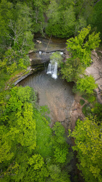 Aerial view of The Herisson waterfalls cascading into a clear pool surrounded by dense green forest and rocky paths in Menetrux-en-Joux, Bourgogne-Franche-Comte, France.