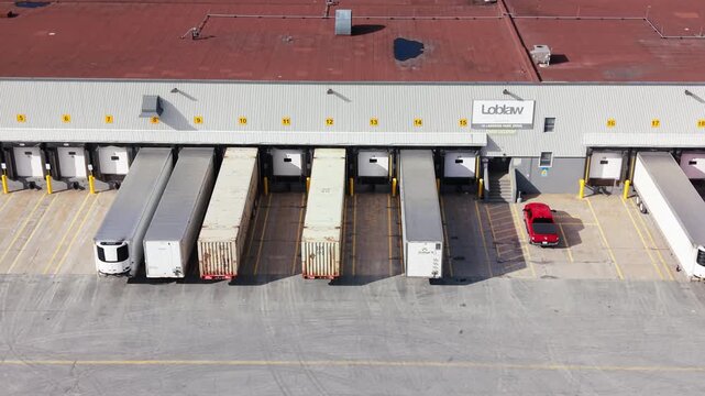 From above, discover a vibrant logistics hub in Halifax, Nova Scotia, where trucks efficiently load and unload shipments at modern docks under clear skies
