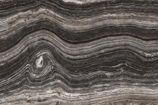 Polished marble surface with flowing layered veins in black gray and beige tones, natural stone texture with curved striations and organic pattern, elegant architectural material